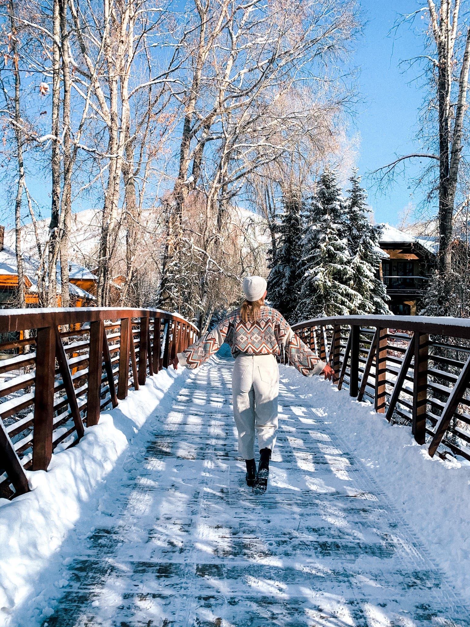 woman enjoying snowmass village in the winter season crossing a bridge on a walking trail with snow and aspen trees