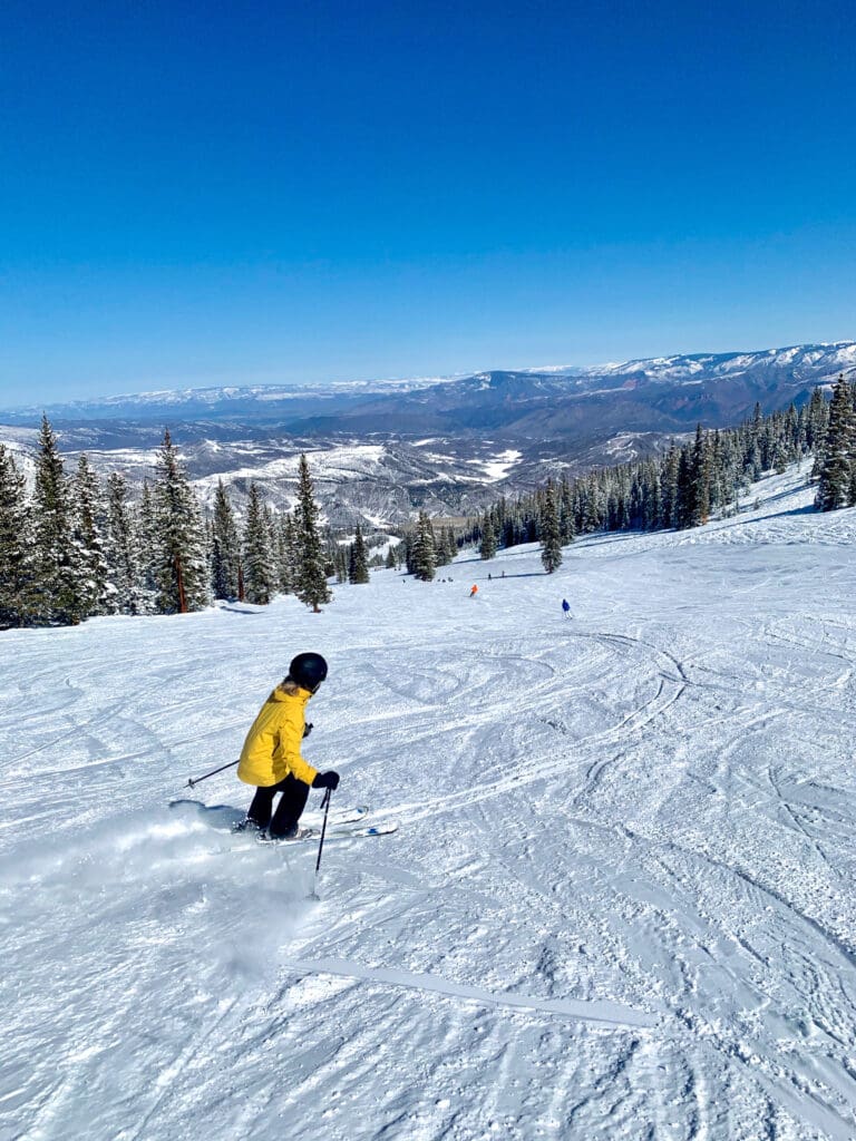 woman skiing down the mountain in snowmass village colorado with beautiful views of the rocky mountains in the roaring fork valley