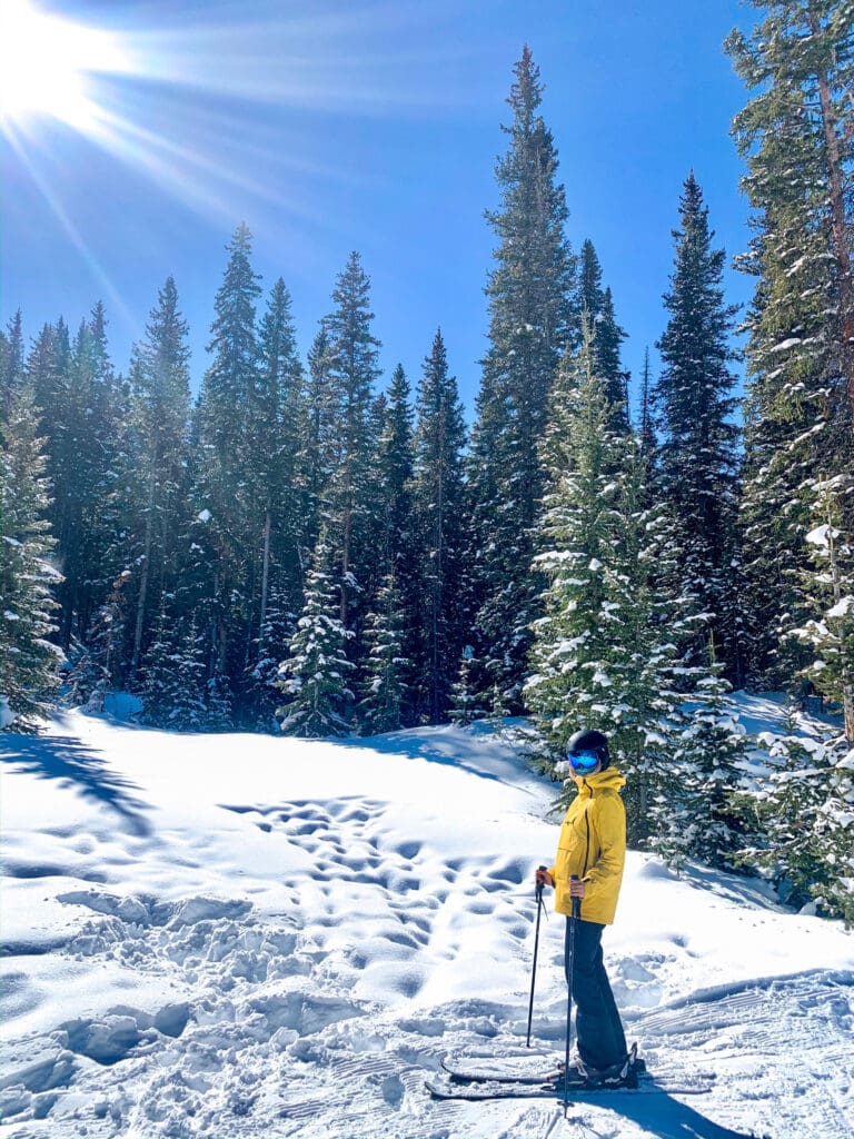 woman skiing in snowmass village colorado in a powder field with trees and fresh snow