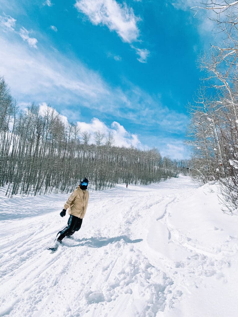 snowboarder in snowmass village colorado shredding at the ski resort in a field of fresh snow and powder surrounded by aspen trees and clear blue skies